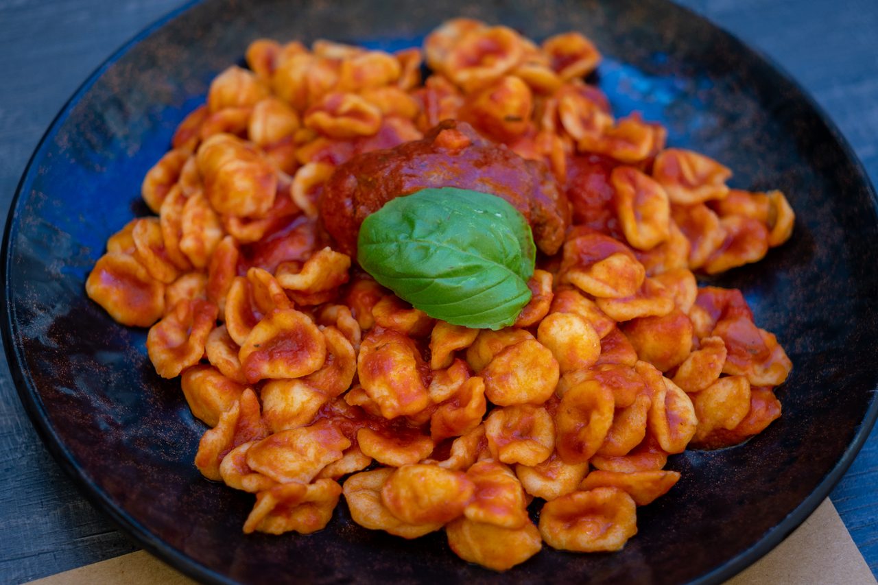 Orecchiette al sugo di pomodoro con polpetta e basilico su piatto nero, tavolo in legno, La Locanda dell'Elfo