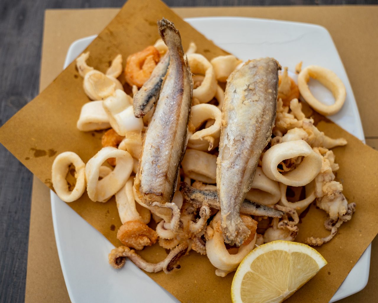 Calamari, gamberi e due pesci fritti su carta paglia in piatto bianco con limone, La Locanda dell'Elfo